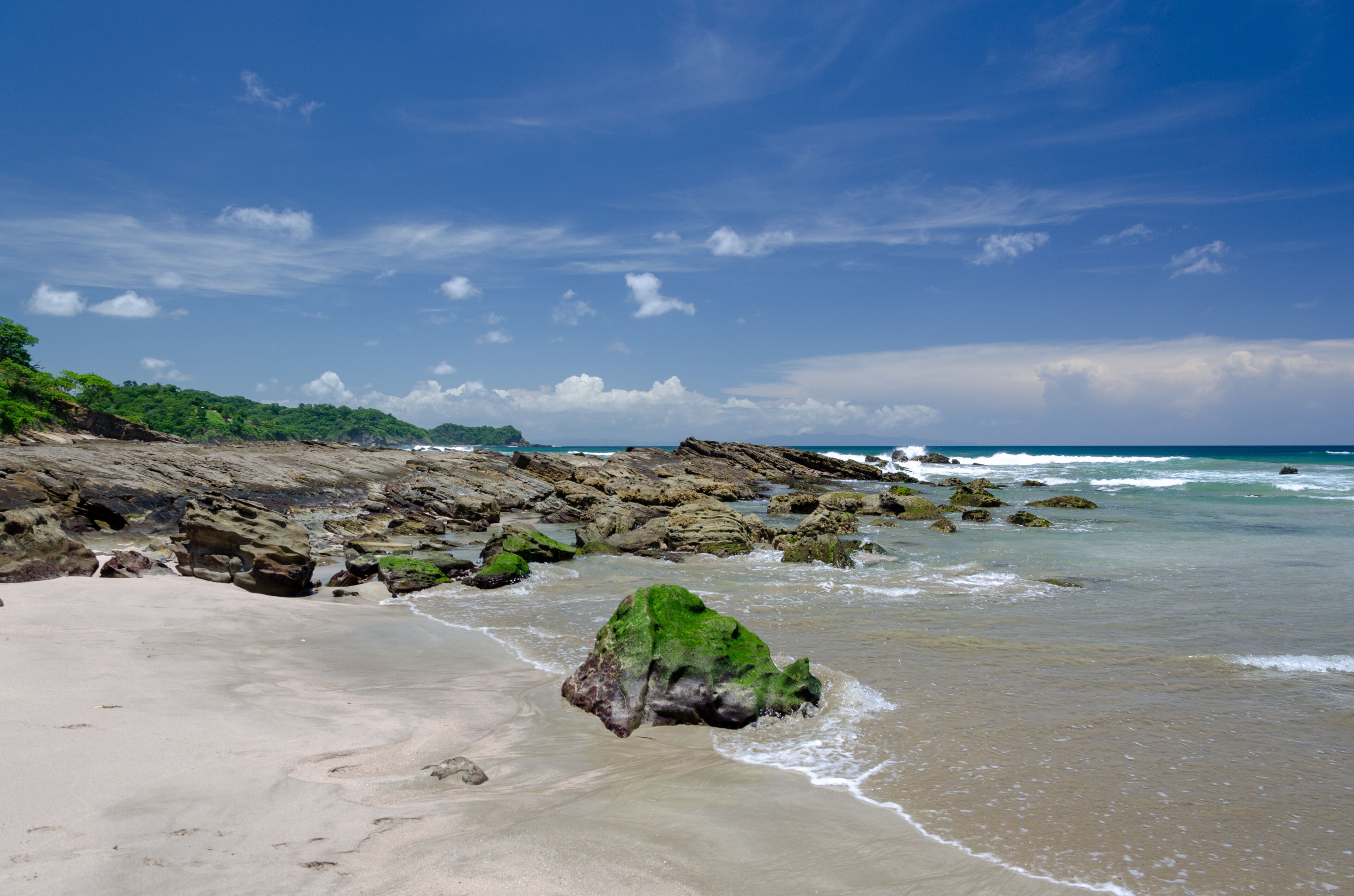 A sandy beach with rocky outcrops and waves crashing onto the shore.
