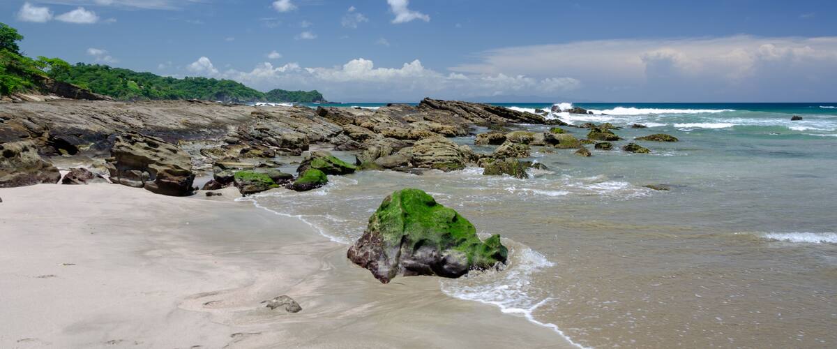A sandy beach with rocky outcrops and waves crashing onto the shore.