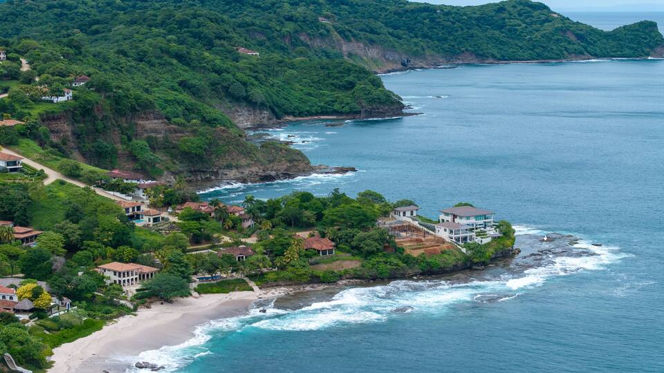 A coastal landscape with lush greenery, a sandy beach, and houses along the cliffside.