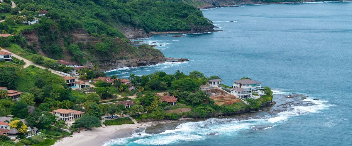 A coastal landscape with lush greenery, a sandy beach, and houses along the cliffside.