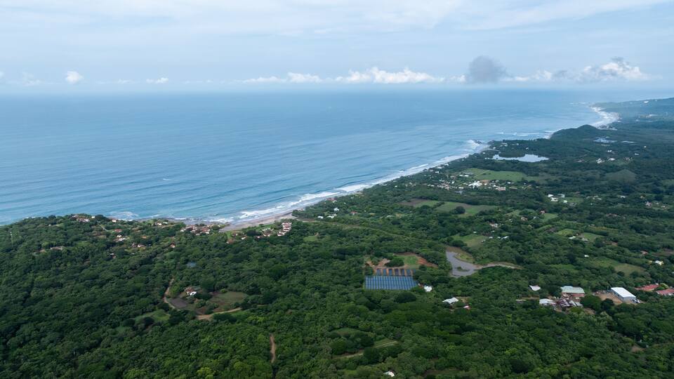 A coastal landscape with dense greenery, a beach, and scattered buildings.