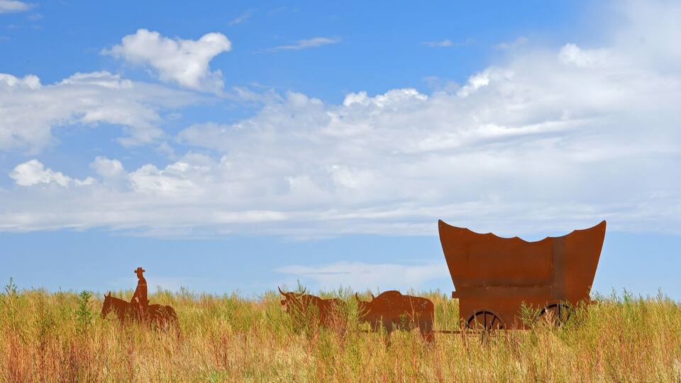 A rusted metal structure in a grassy field under a blue sky.