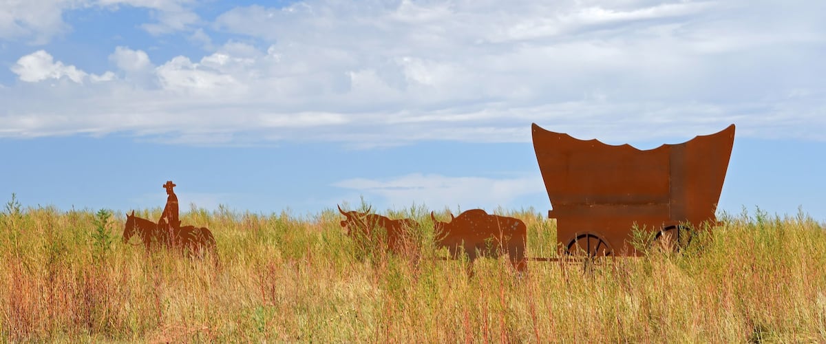 A rusted metal structure in a grassy field under a blue sky.