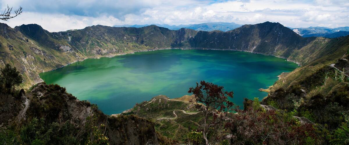 A large, circular lake surrounded by rugged mountains and dense vegetation.