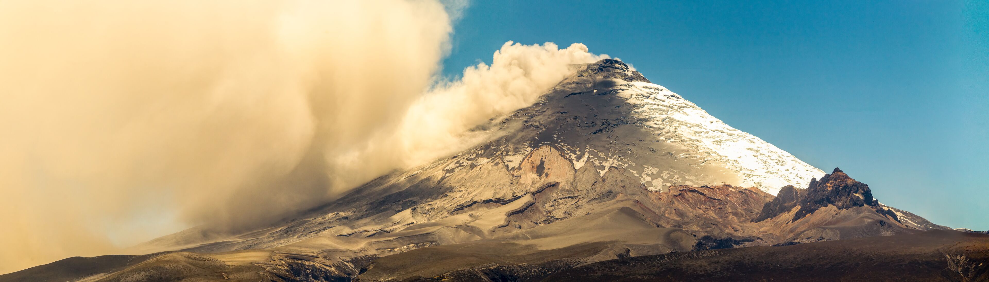 A snow-capped mountain with a prominent peak and a cloud of dust or smoke rising from its base.