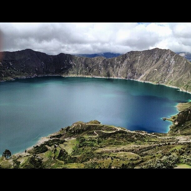 Un lago extenso y tranquilo rodeado de montañas escarpadas y una carretera sinuosa.