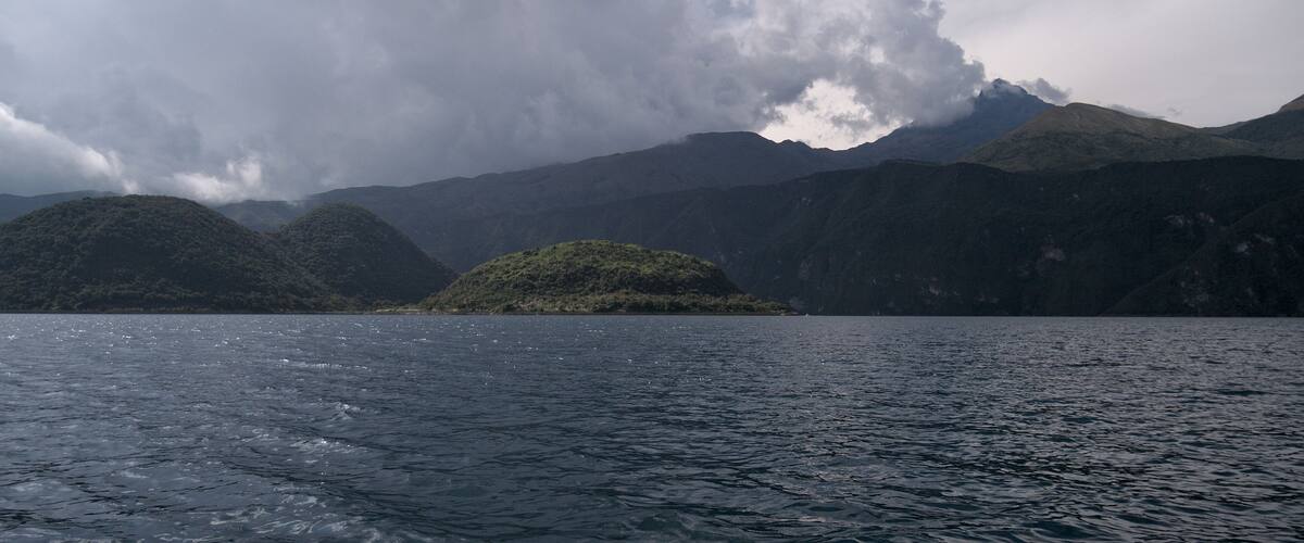 A body of water with a small island and mountains in the background.