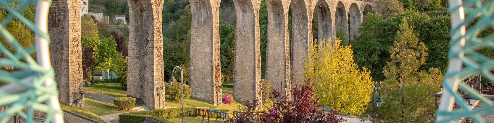 A stone viaduct with multiple arches over a park with playground equipment.