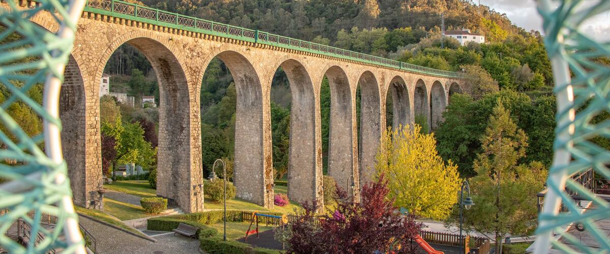 A stone viaduct with multiple arches over a park with playground equipment.