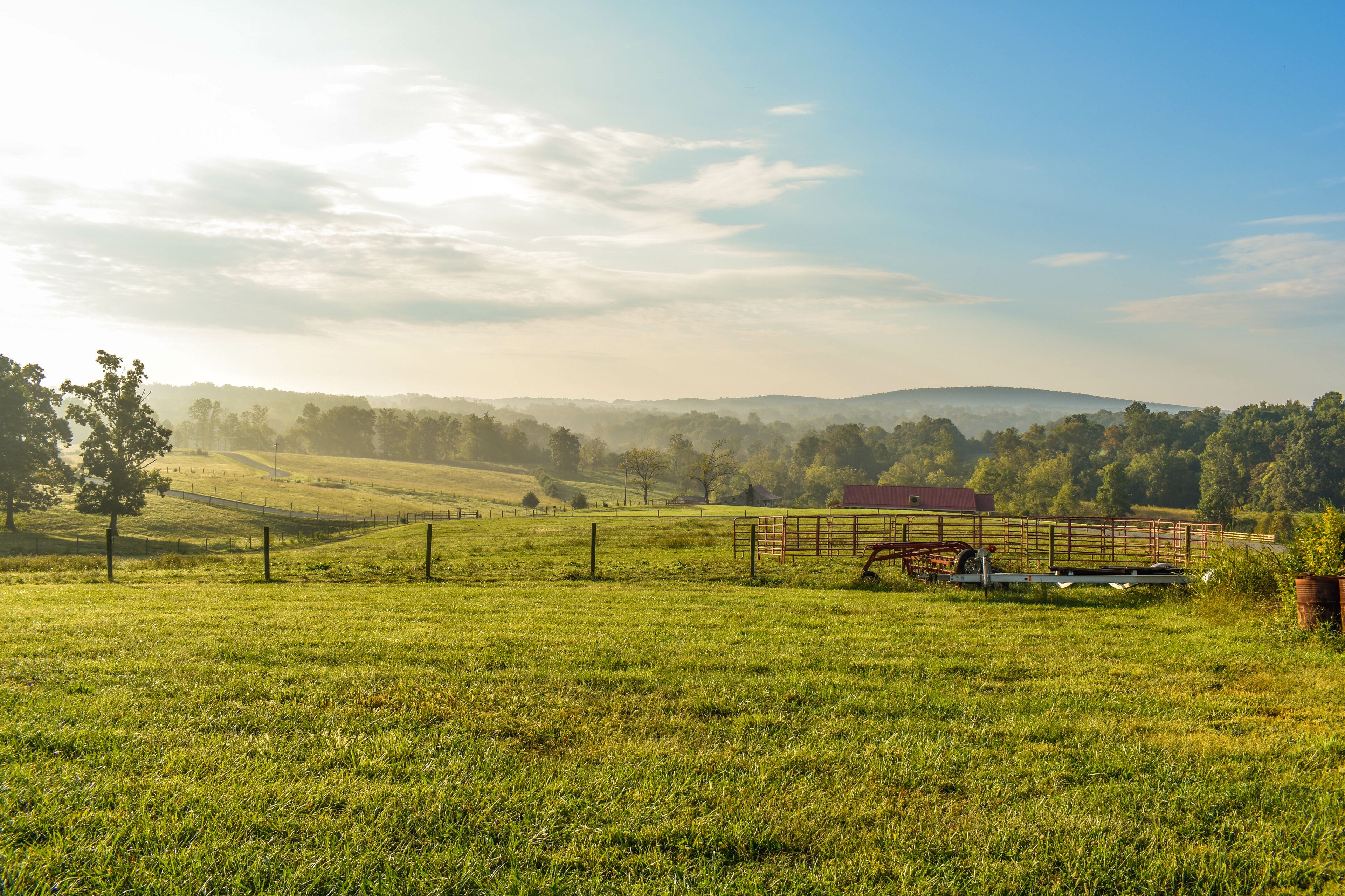 A green field with a red barn, a fence, and distant hills.