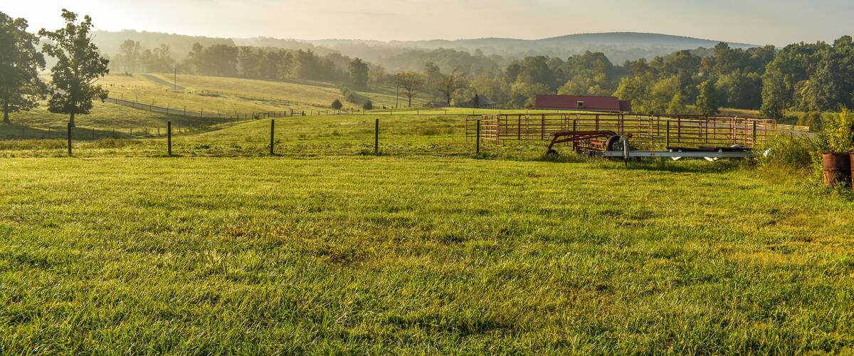 A green field with a red barn, a fence, and distant hills.