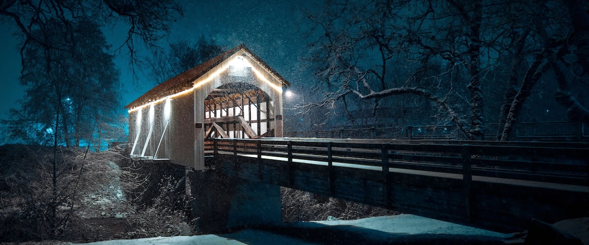 A snow-covered bridge with a lit structure on the left.