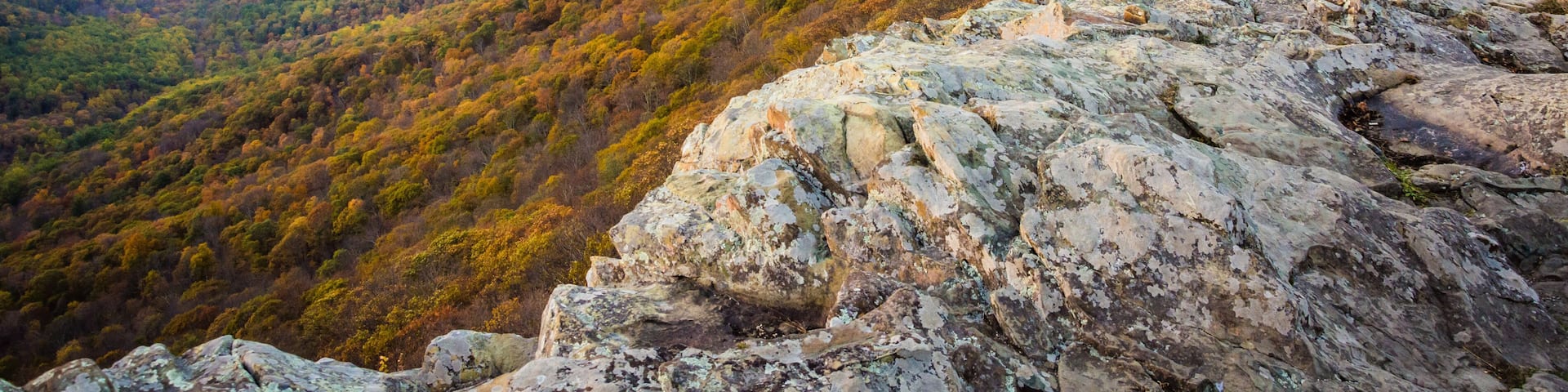 A mountainous landscape with autumn foliage, rocky outcrops, and a distant view of a valley.