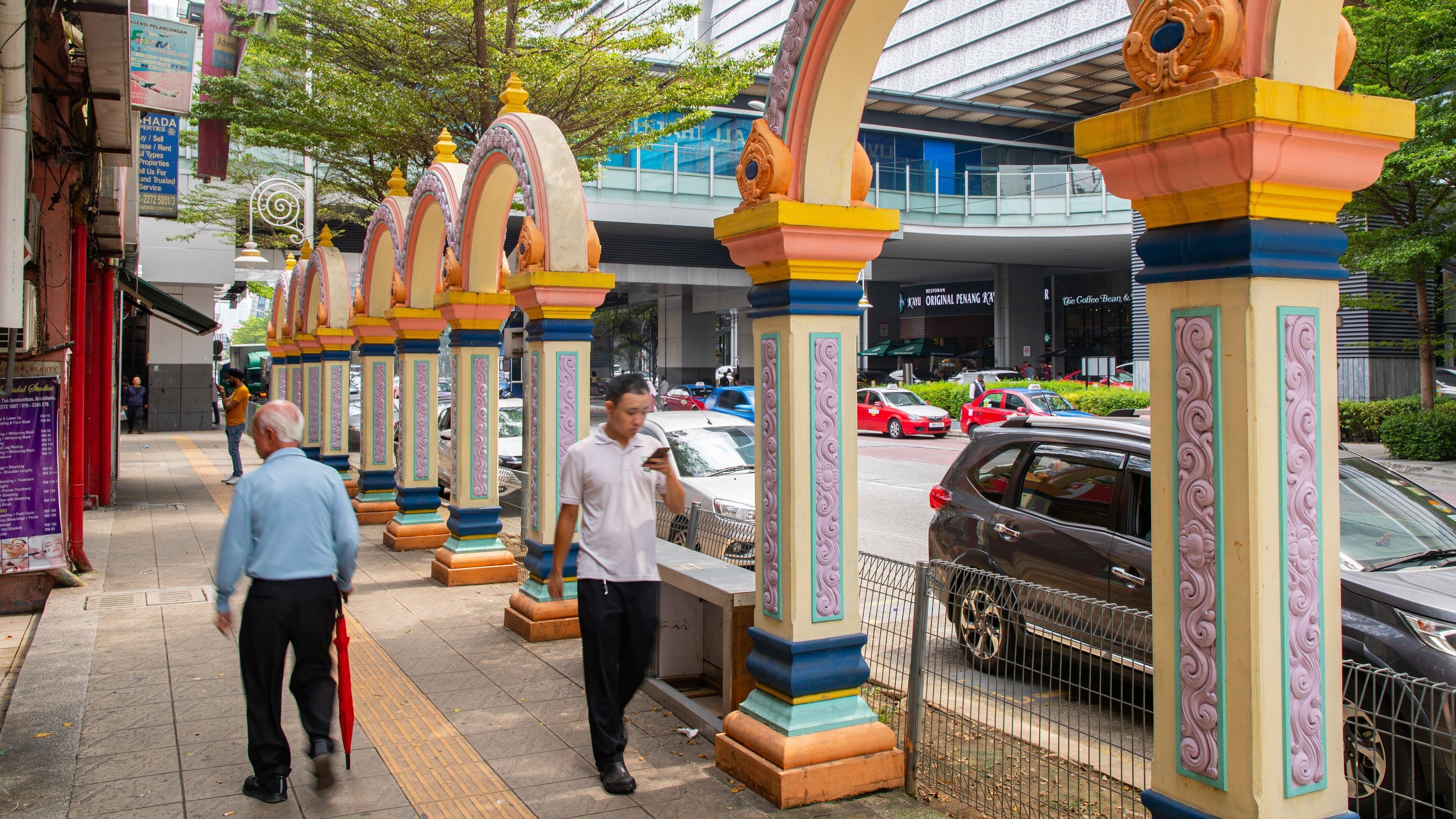 A pedestrian walkway with colorful, ornate pillars and a modern building in the background.