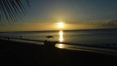 A beach at sunset with a boat and people in the water.
