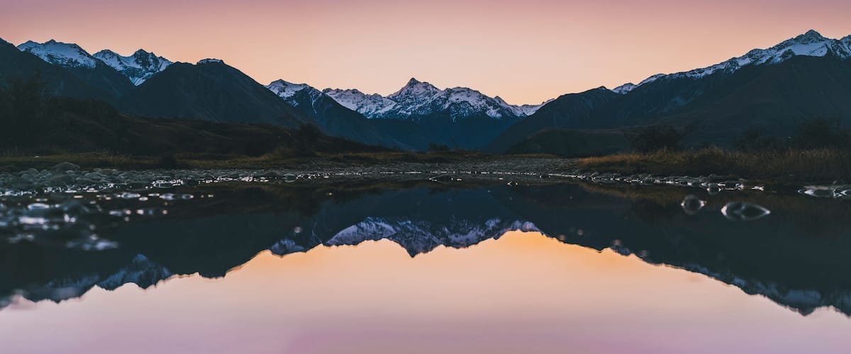A mountain range reflected in a calm lake with a gradient sky.