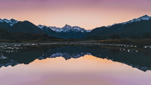A mountain range reflected in a calm lake with a gradient sky.
