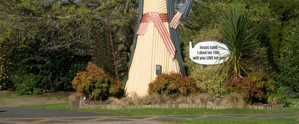 A large statue of a man in a robe holding a staff, surrounded by greenery and a sign with a quote.