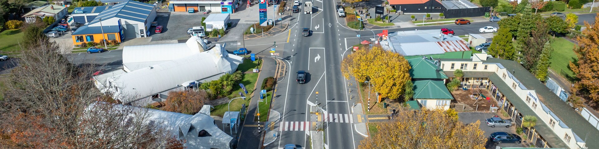 Vista aérea de un pueblo con una avenida principal, casas residenciales y un edificio grande de color blanco con techo azul.