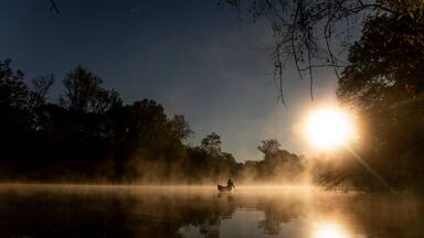 A misty lake at sunrise with a person paddling a canoe.