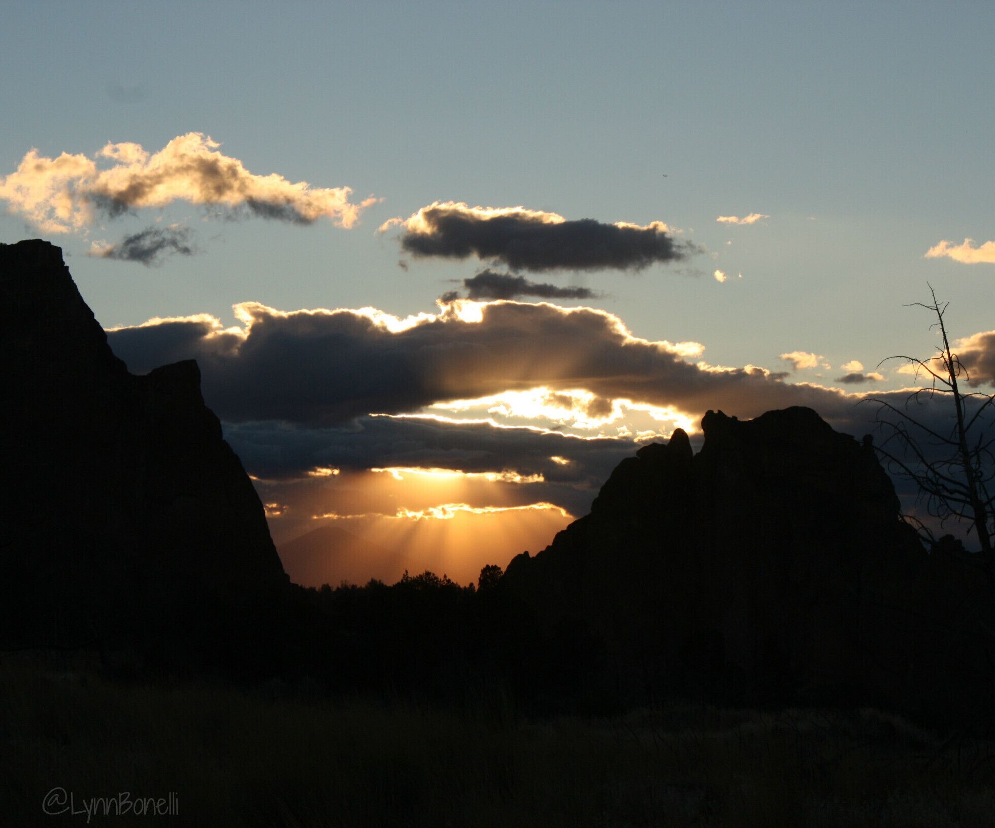 A sunset over a mountainous landscape with silhouetted peaks and scattered clouds.