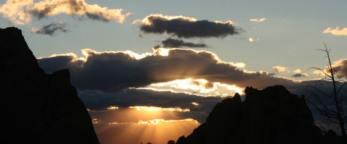 A sunset over a mountainous landscape with silhouetted peaks and scattered clouds.