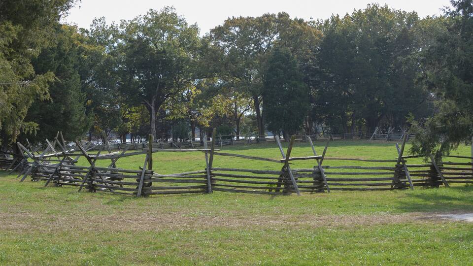 A wooden fence in a grassy field with trees in the background.