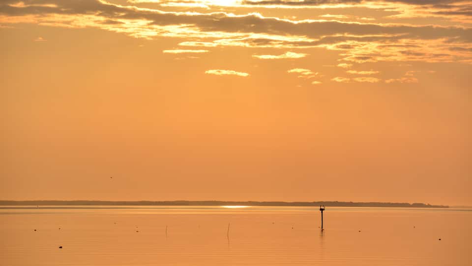A sunset over a calm body of water with a distant shoreline and a solitary pier.
