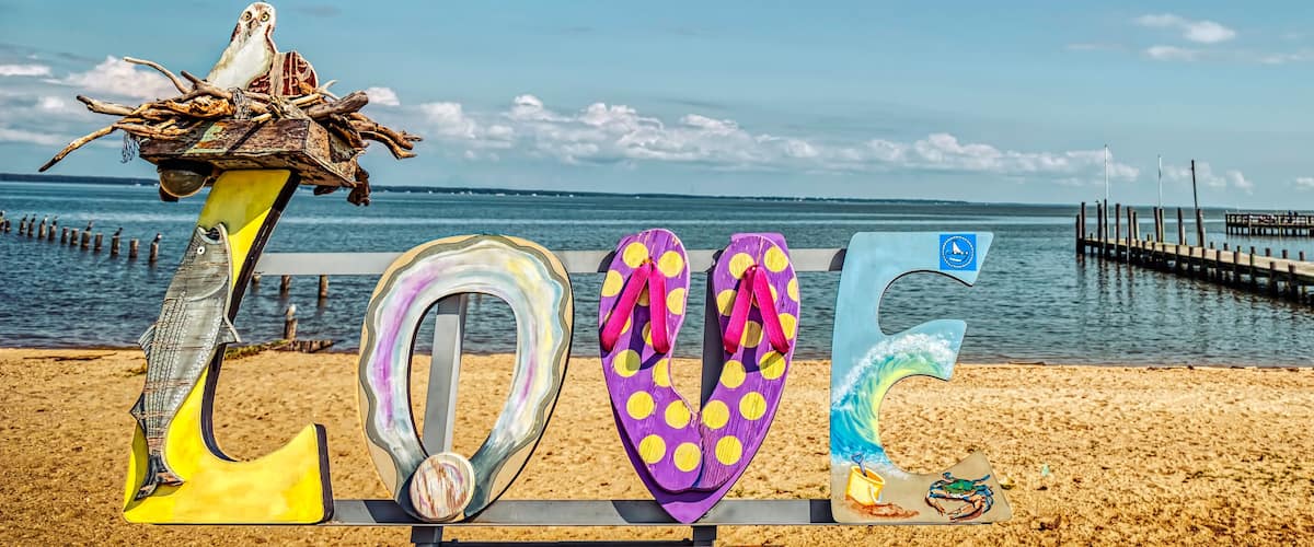 A beach with a wooden bench, colorful flip-flops, and a pier in the background.