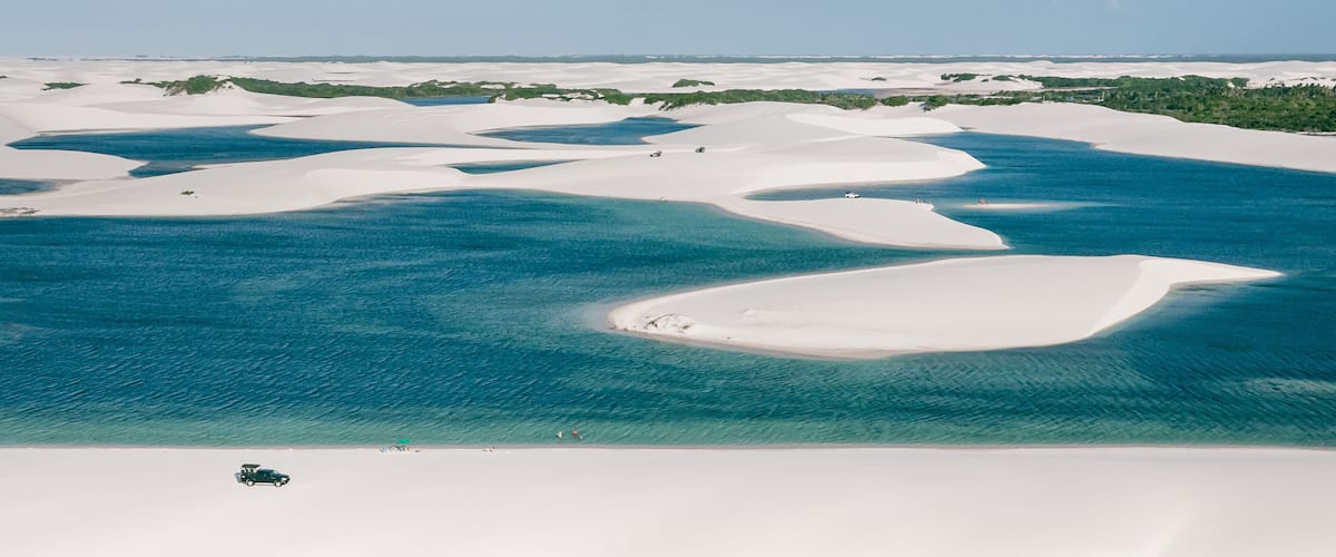 A coastal landscape with white sand dunes and clear blue waters.