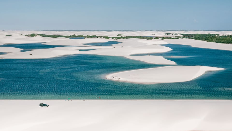 A coastal landscape with white sand dunes and clear blue waters.