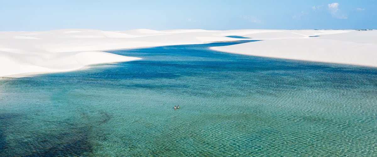 A clear blue river winding through white sand dunes.