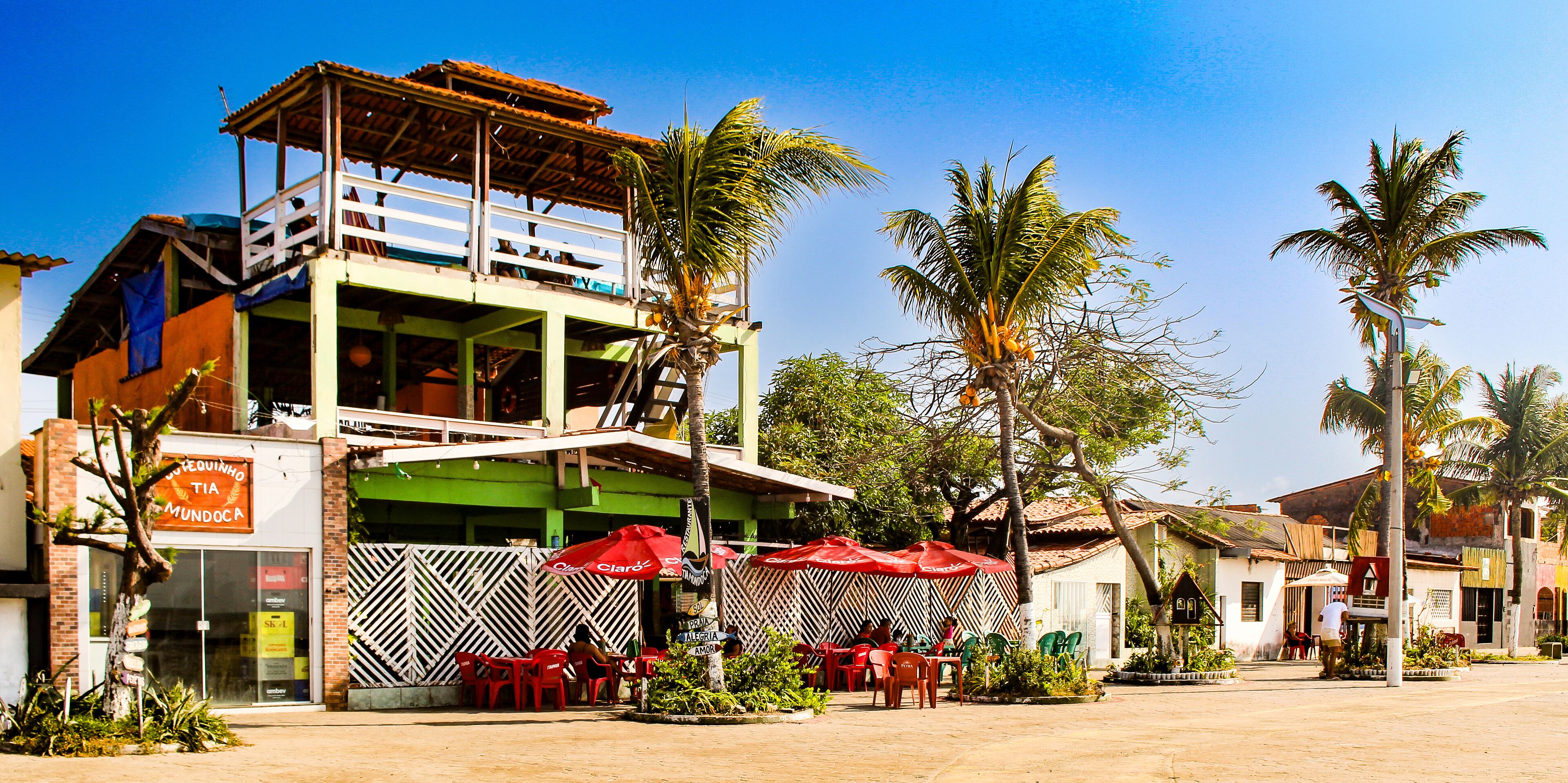 A two-story building with a green and white facade, a balcony, and red umbrellas.