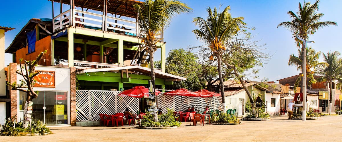 A two-story building with a green and white facade, a balcony, and red umbrellas.