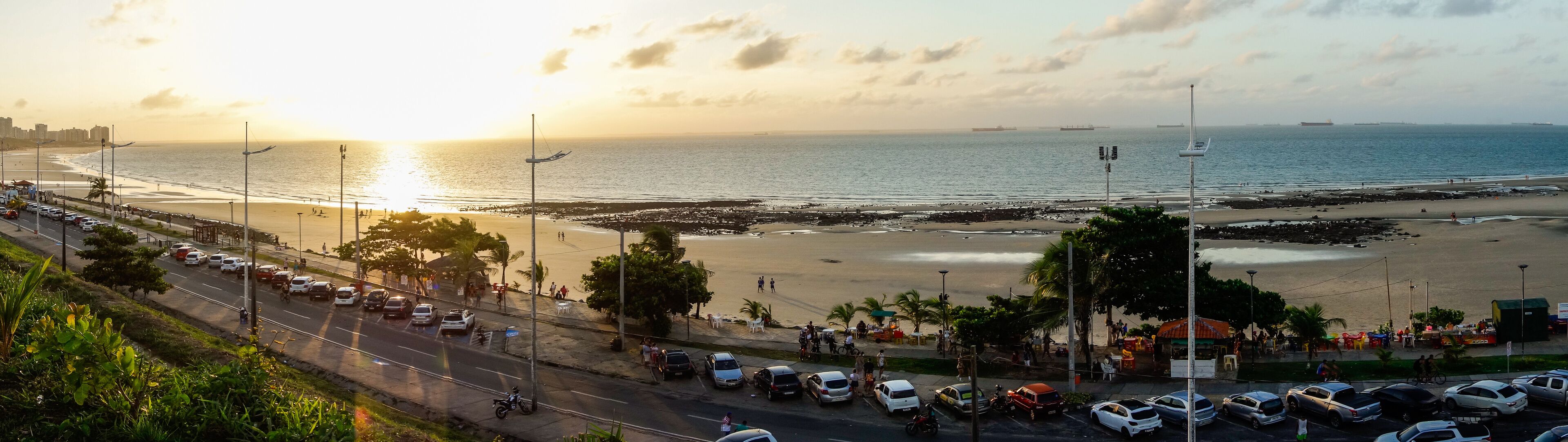 A coastal road with parked cars and a beach in the background.