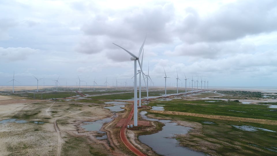 A wind farm with multiple wind turbines in a flat landscape with a road and water bodies.