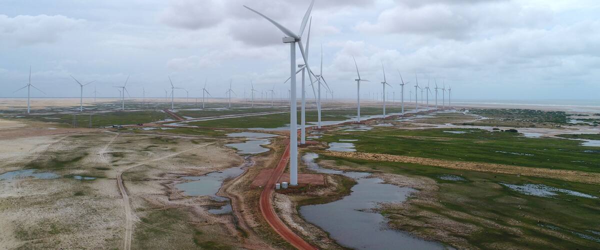 A wind farm with multiple wind turbines in a flat landscape with a road and water bodies.
