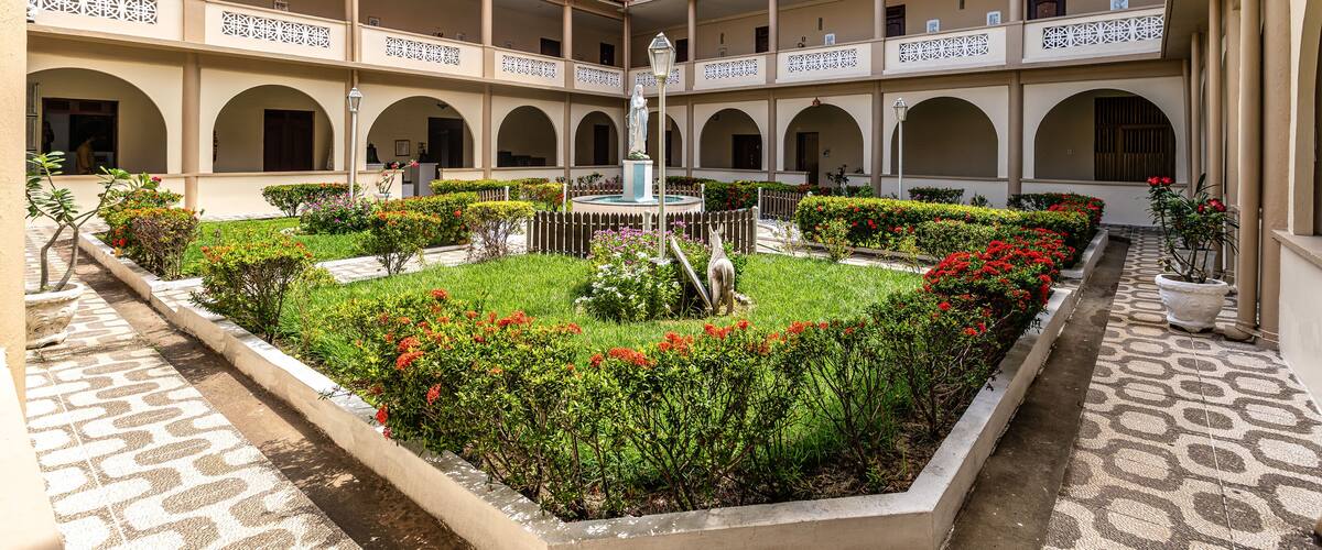 A courtyard with a central fountain, surrounded by greenery and a patterned walkway.