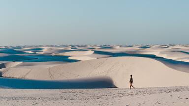 Vasta paisagem desértica com dunas de areia ondulantes e uma pessoa caminhando ao longe.