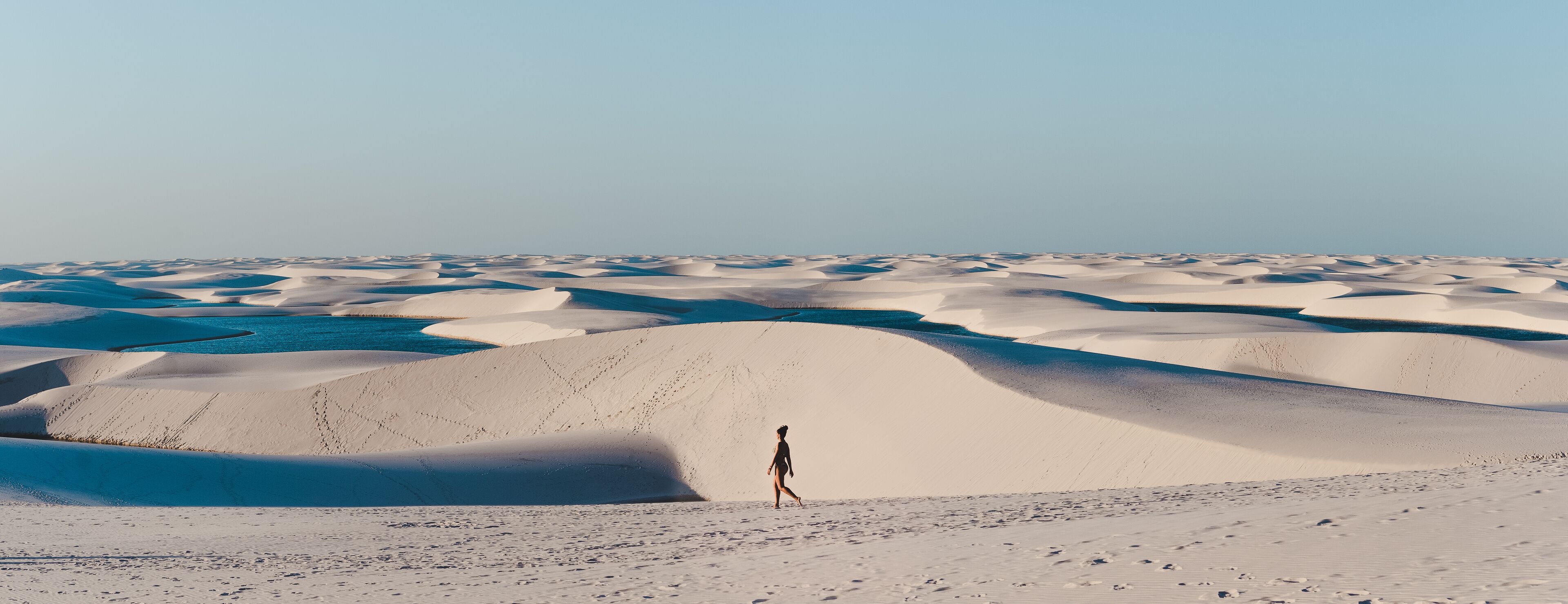 A vast desert landscape with rolling sand dunes and a person walking in the distance.