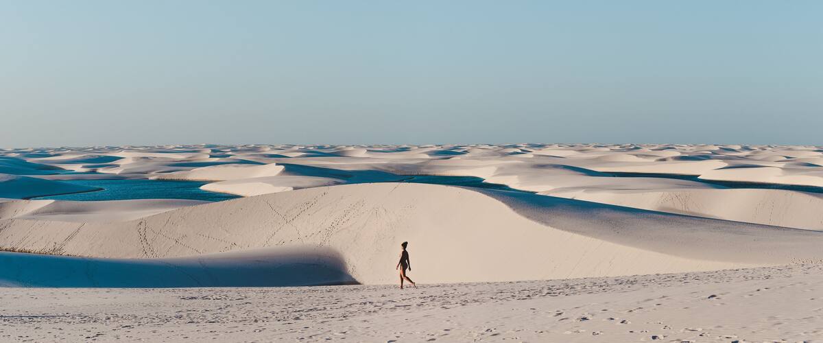 A vast desert landscape with rolling sand dunes and a person walking in the distance.