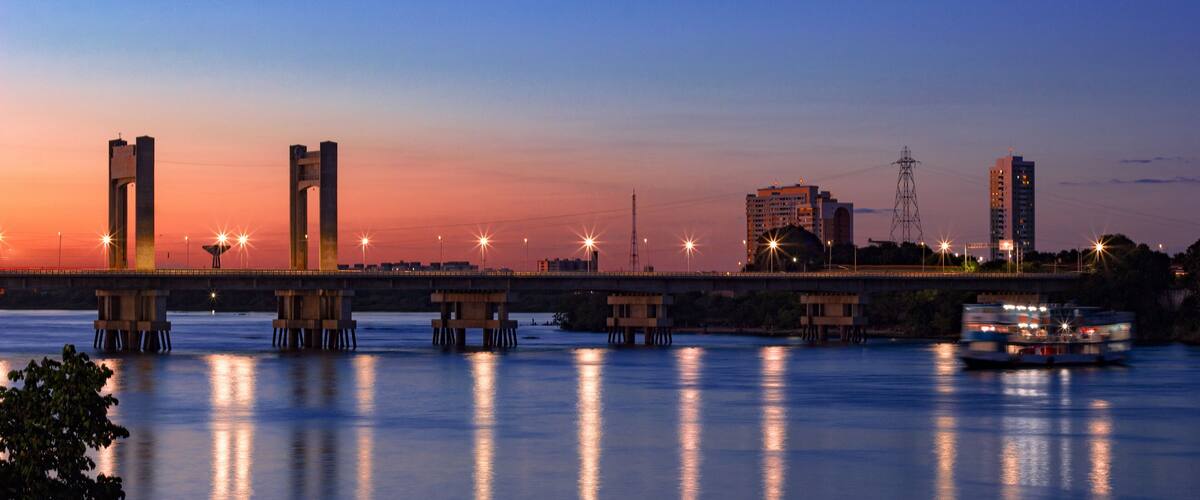A river at dusk with a bridge, buildings, and a boat.