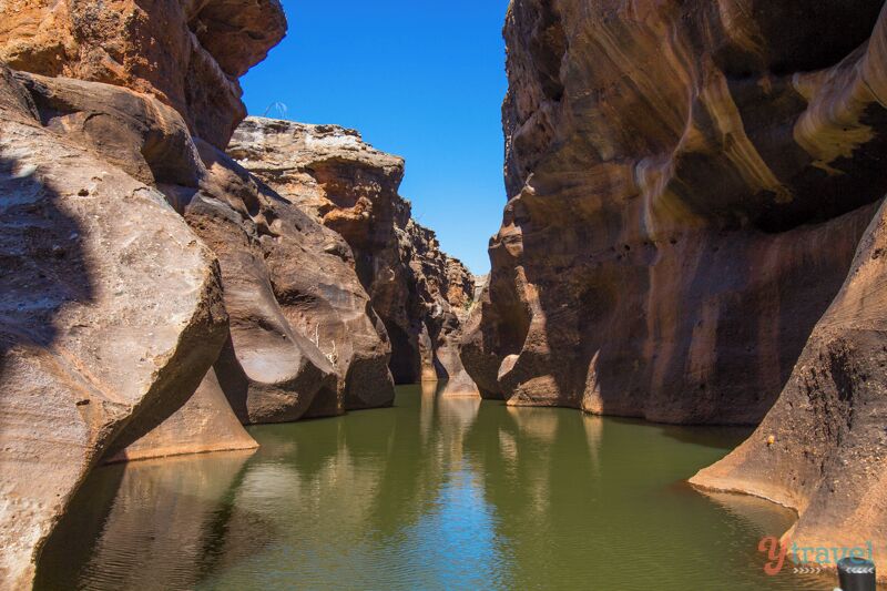 A canyon with steep rock walls and a calm green pool at the bottom.