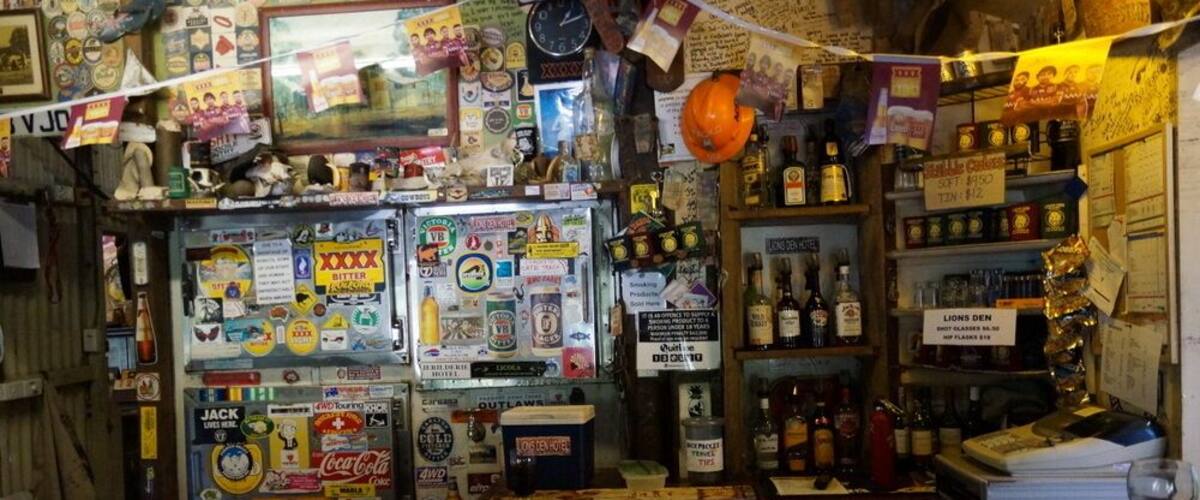 A cluttered bar with various liquor bottles and a refrigerator covered in stickers.