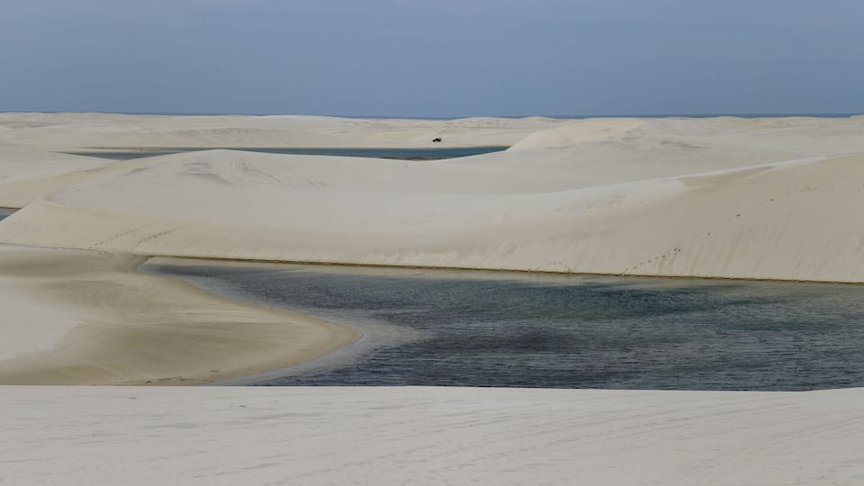 A vast desert landscape with sand dunes and a small body of water.