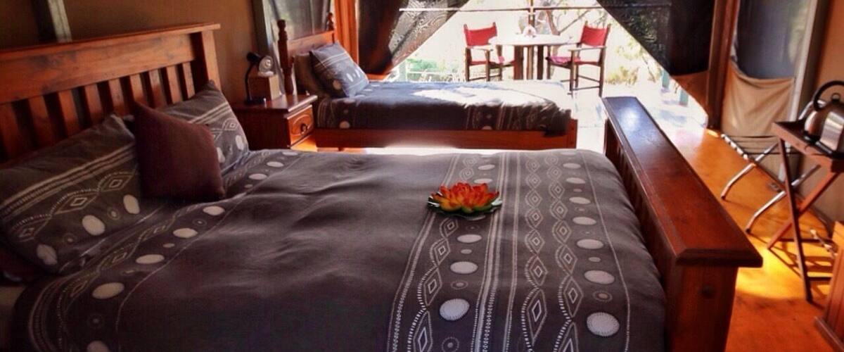 A tented accommodation with a bed, a bench, and a table.