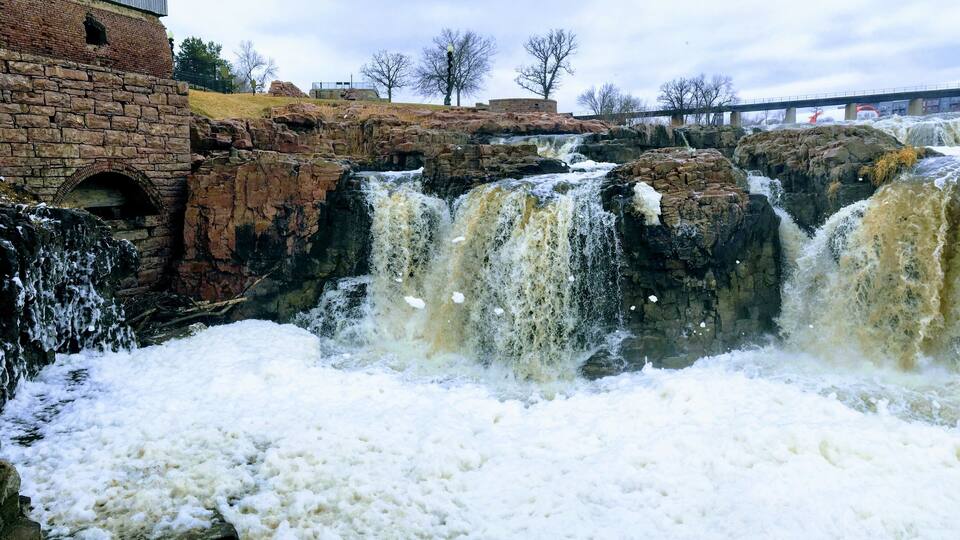 A multi-tiered waterfall with a stone building in the background.