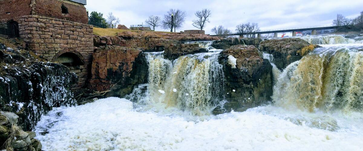 A multi-tiered waterfall with a stone building in the background.