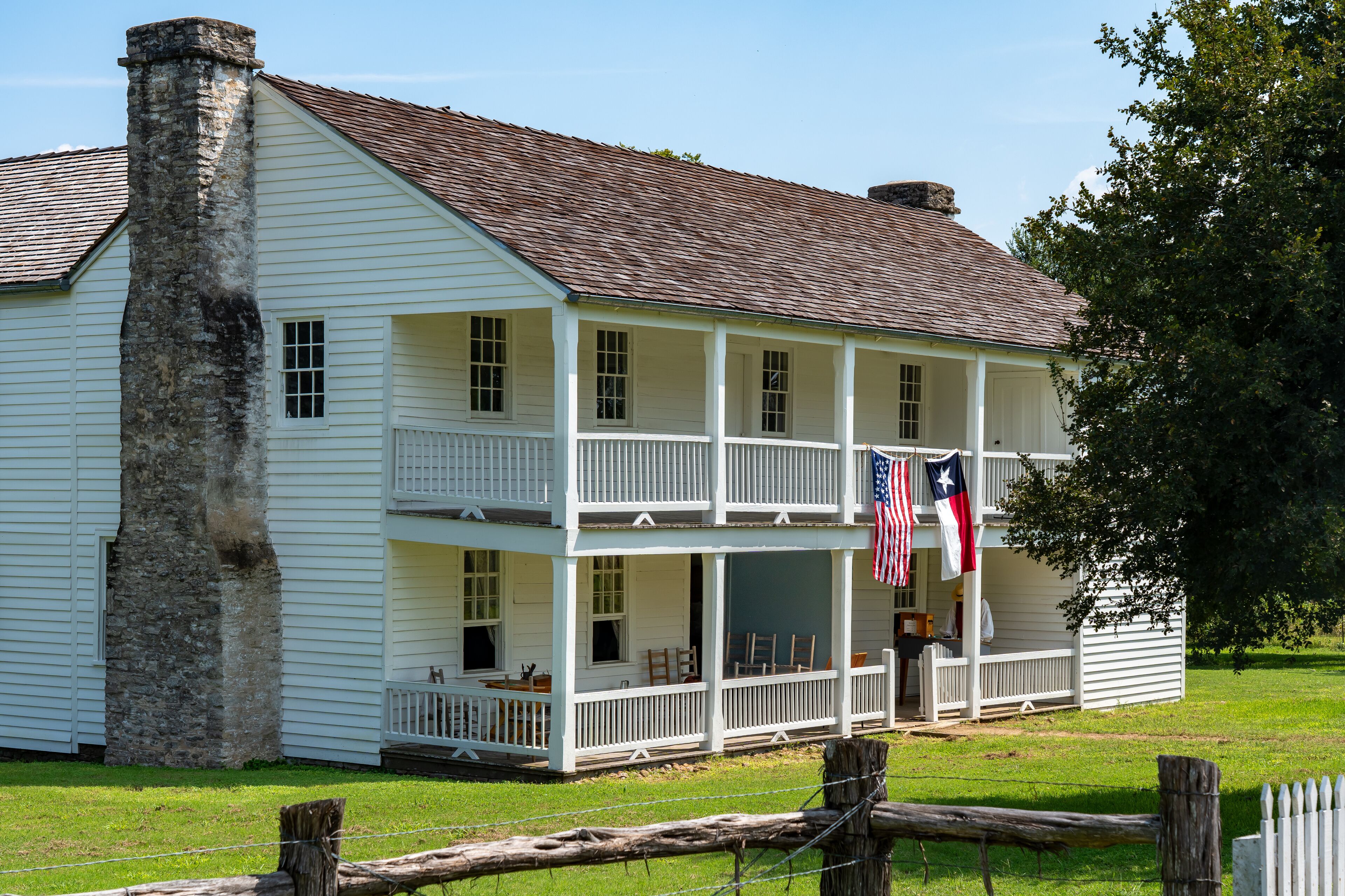A white colonial-style house with a chimney, a porch, and two flags.