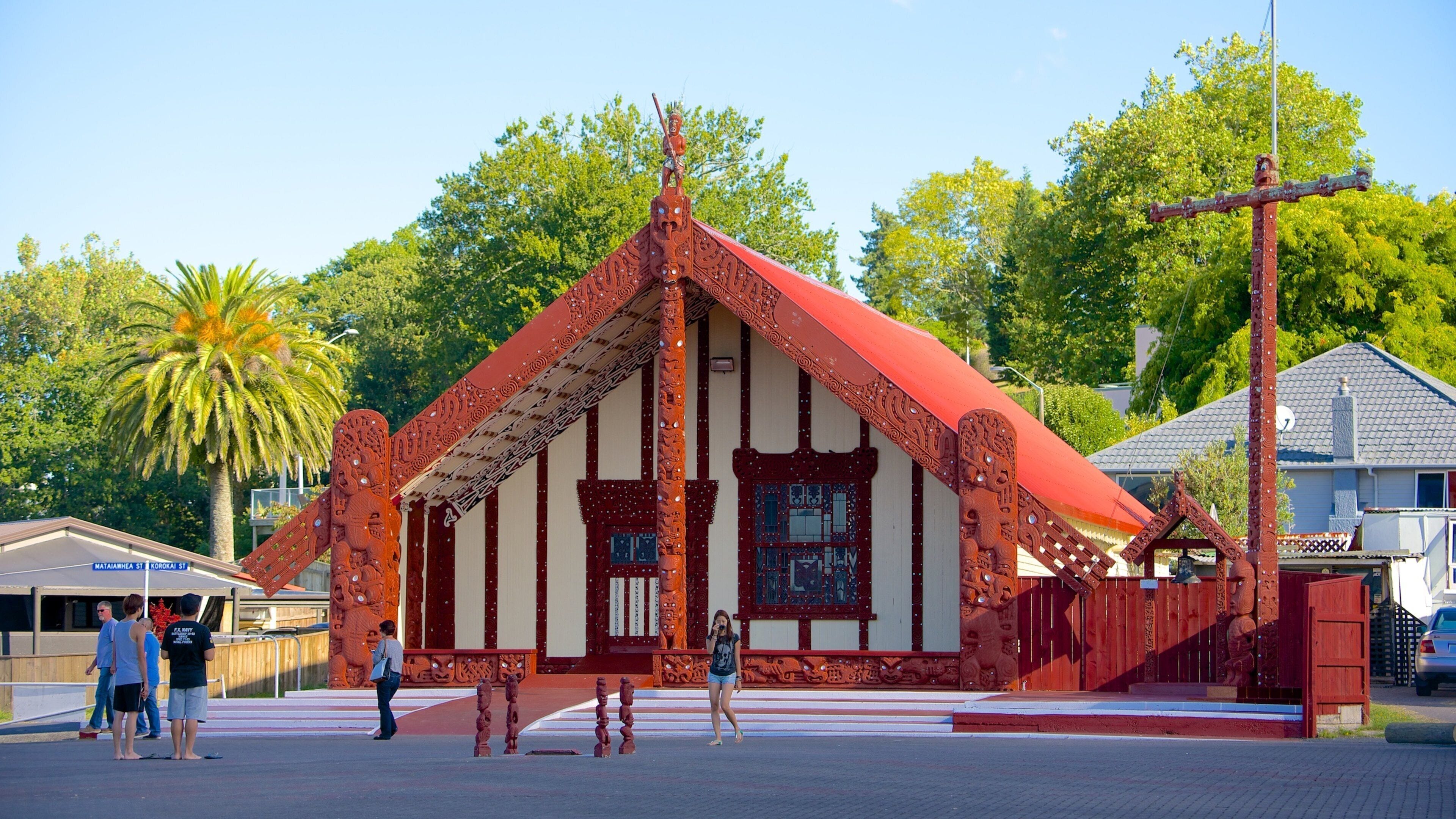 A traditional wooden building with intricate carvings and a red roof, surrounded by lush green trees and a clear blue sky.